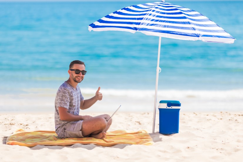 Man on beach sitting under shade of umbrella