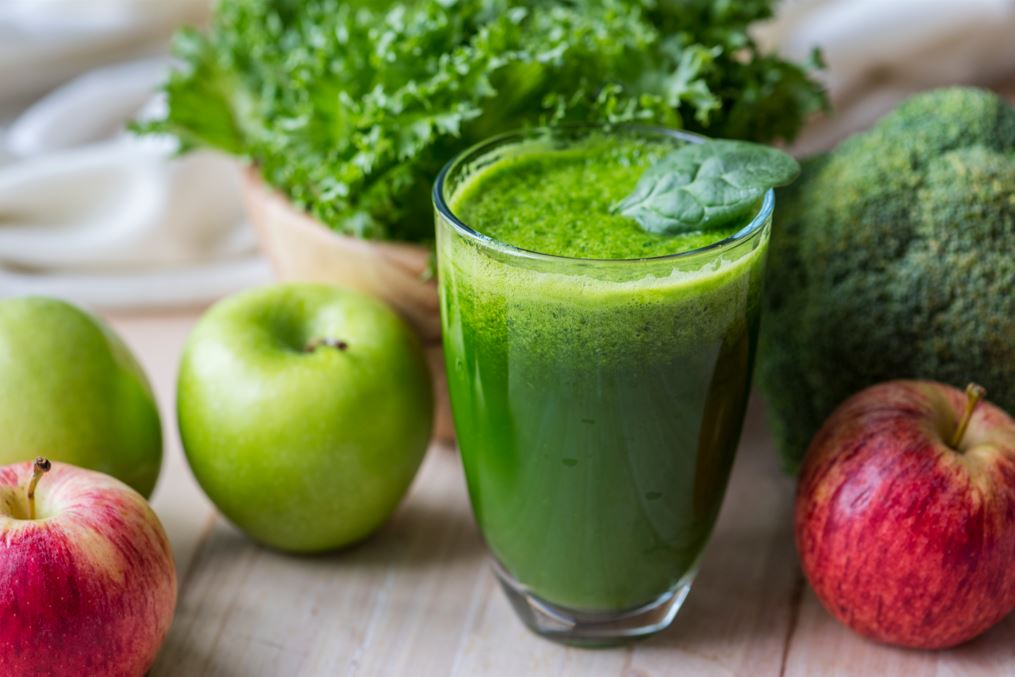 green smoothie in glass with apples, spinach and broccoli nearby