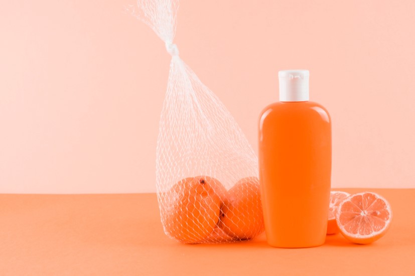 Bottle of suntan lotion with bag of oranges beside