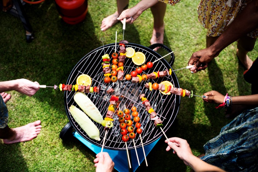 Friends holding skewers of meat and veggies over open grill